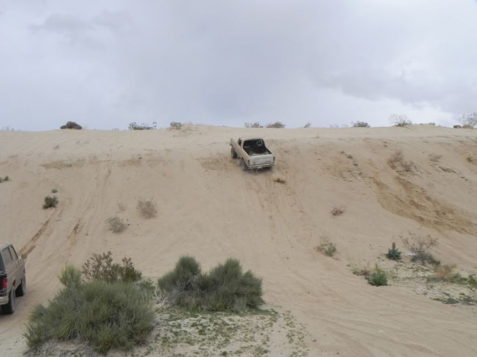 Topless 4x4 climbing a steep desert sand hill with tire tracks down the face