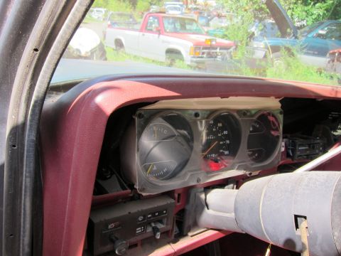 1991 Ford LTD Crown Victoria - Interior view of a car's dashboard with gauges and radio, with other vehicles visible in the junkyard beyond.
