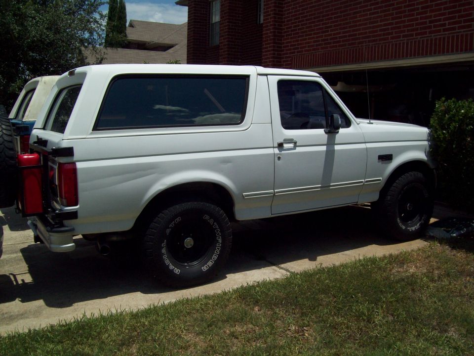 White Ford Bronco SUV, side/rear view, black wheels with white-letter tires, red can on rear carrier