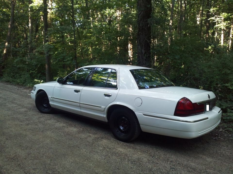 White 2000 Mercury Grand Marquis parked on a dirt road with trees in the background