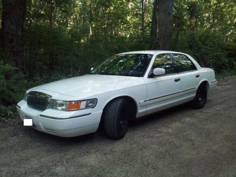 2000 Mercury Grand Marquis - A white 2000 Mercury Grand Marquis is parked on a dirt path surrounded by trees.