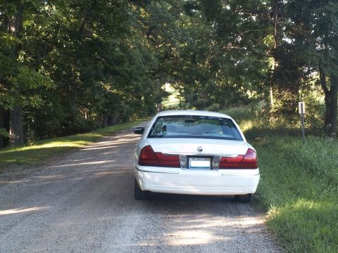 2000 Mercury Grand Marquis - A white 2000 Mercury Grand Marquis is parked on a gravel road surrounded by trees.