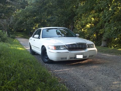 2000 Mercury Grand Marquis - A white 2000 Mercury Grand Marquis is parked on a gravel road surrounded by trees.