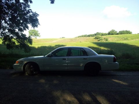 2000 Mercury Grand Marquis - A light-colored sedan is parked on a dirt road with a grassy hill in the background.