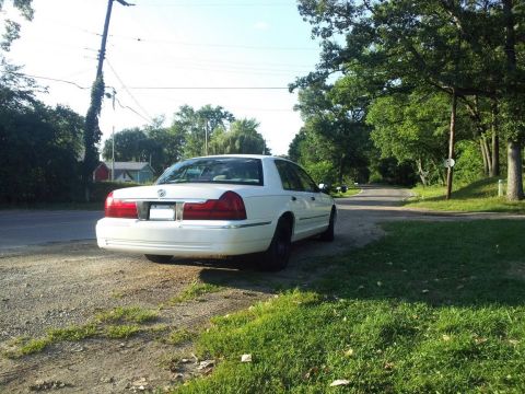2000 Mercury Grand Marquis - A white 2000 Mercury Grand Marquis is parked on the side of a tree-lined road.