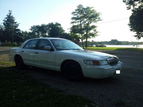 2000 Mercury Grand Marquis - A white 2000 Mercury Grand Marquis is seen parked near a body of water on a sunny day.