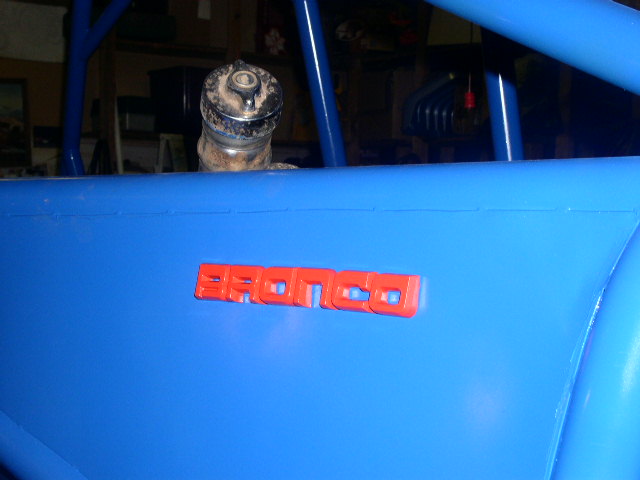 Blue vehicle side panel with red Bronco badge. Roll cage visible