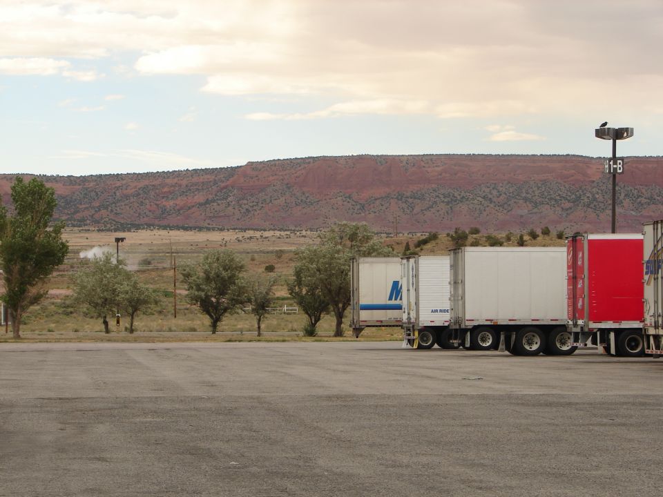 Several semi-truck trailers parked in a lot with a red mesa in the background