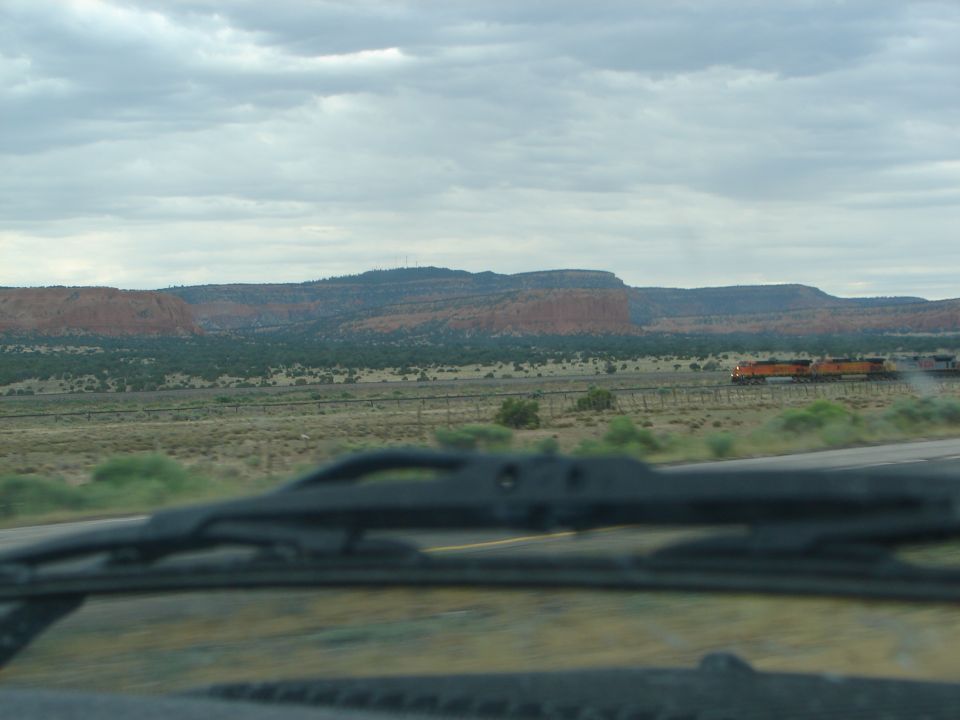 Train moving through desert landscape with red rock formations in background. Shot from inside a vehicle