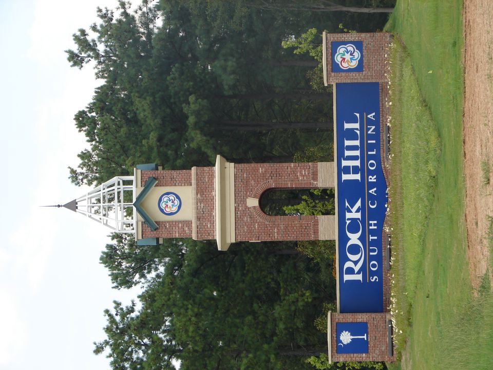 Brick clock tower with white spire and blue sign reading Rock Hill South Carolina