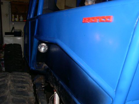 1979 Ford Bronco - A blue off-road vehicle with a roll cage is visible from the side, displaying a red 'BRONCO' badge.
