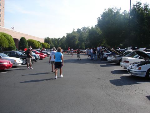 1992 Ford Taurus - Cars parked in a lot with people walking around, some hoods are open.