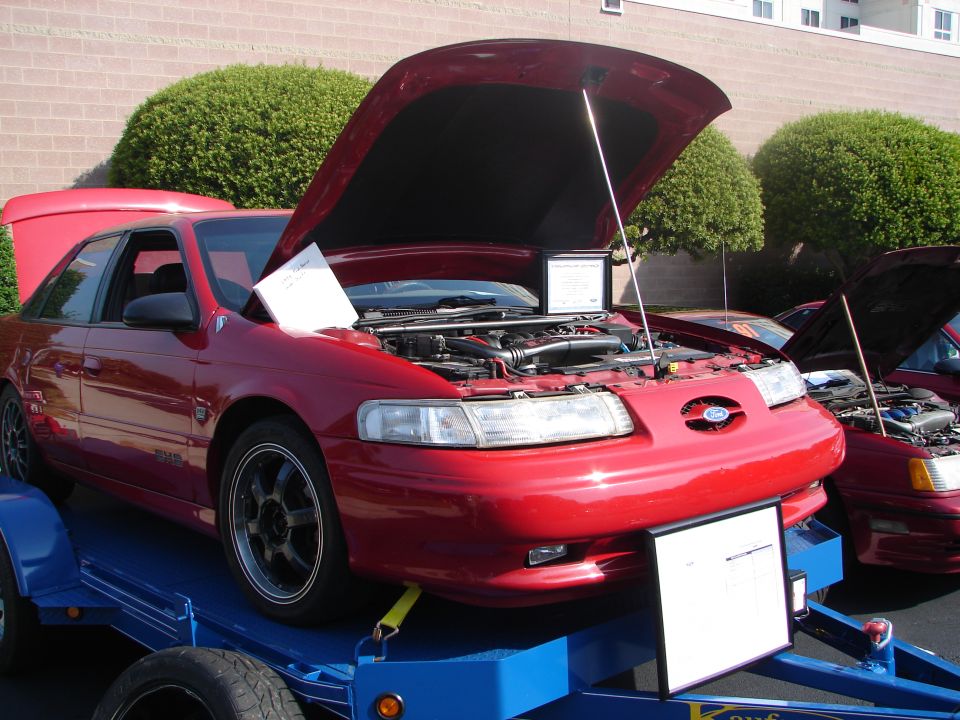 Red sedan on trailer, hood open showing engine. Another red car behind it
