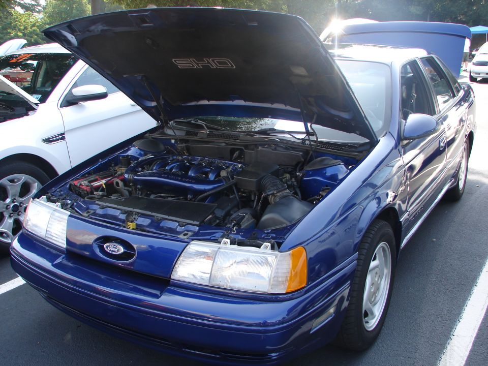 1992 Ford Taurus SHO, blue, hood open showing engine. Another white car is parked next to it