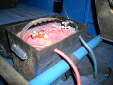 1979 Ford Bronco - Vehicle battery secured in a black box with visible wiring and roll cage components.