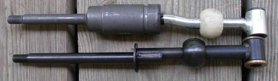 Two metal shift levers, one silver with a white knob, the other black with a black knob, lie on a wooden surface