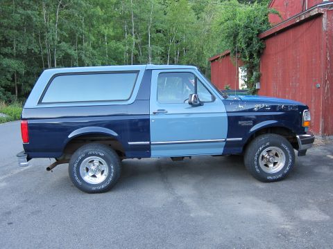 2001 Ford Crown Victoria - A two-tone blue Ford Bronco is parked on asphalt in front of a red wooden building.
