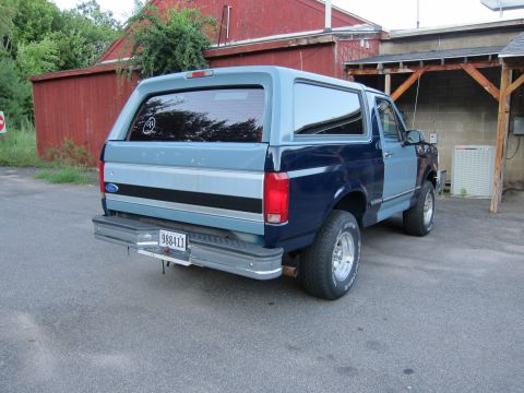 2001 Ford Crown Victoria - The rear of a two-tone blue Ford Bronco is visible, parked outdoors near a red building.