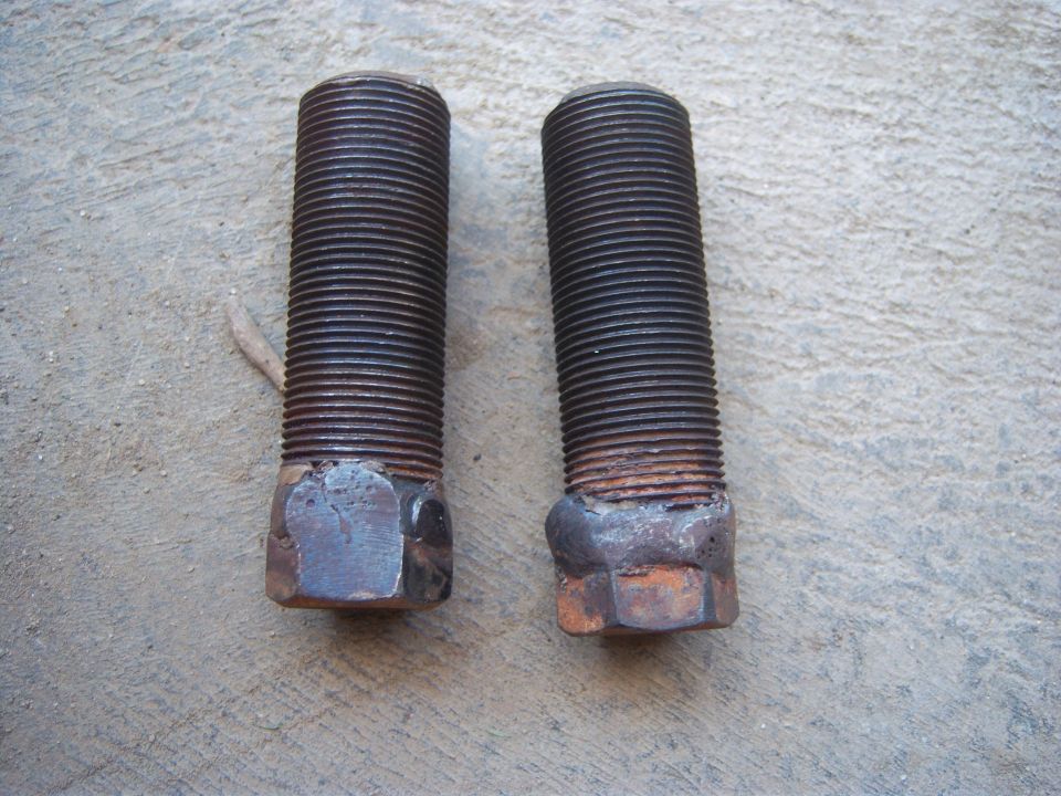 Two rusty threaded bolts with hex heads, lying on a concrete surface