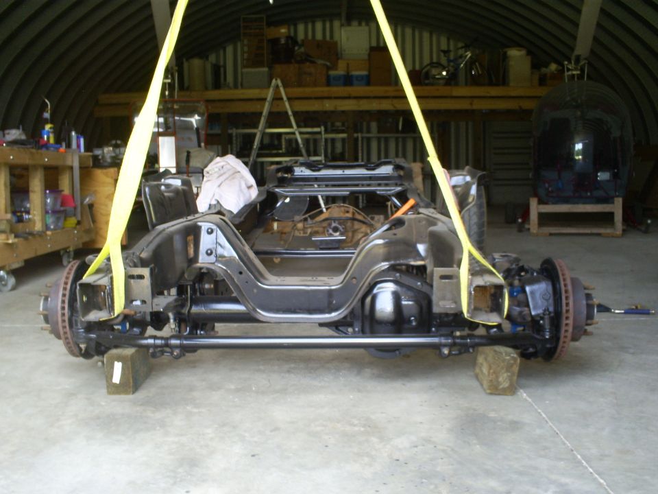 Vehicle frame and suspension assembly lifted by yellow straps, resting on wooden blocks