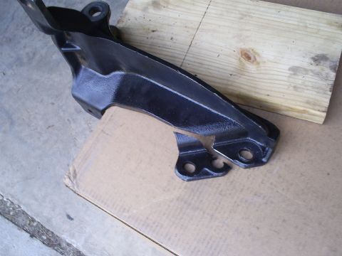 1992 Ford Bronco - A black metal automotive part rests on cardboard and a wooden plank.