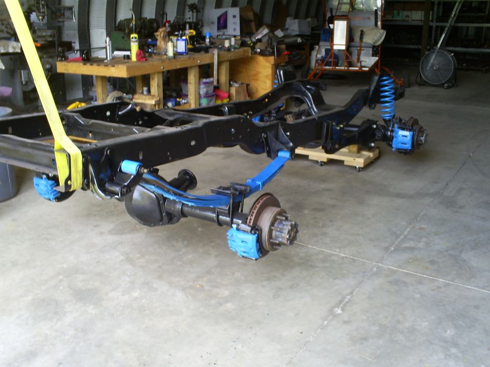 Black vehicle frame with blue suspension components and disc brakes, suspended by yellow straps