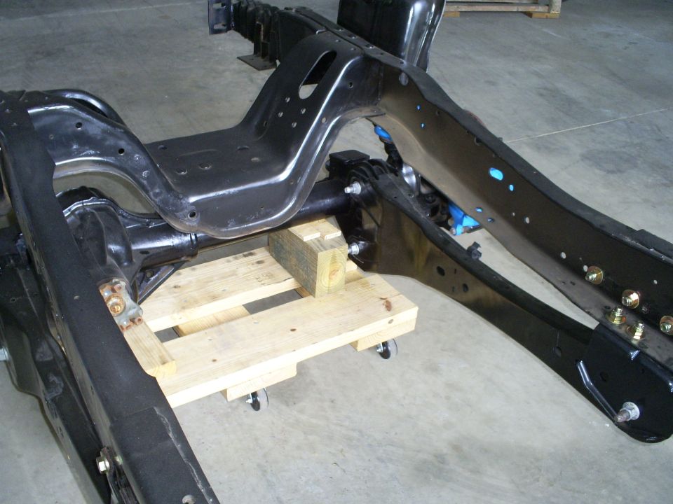 Black vehicle frame and suspension parts on a wooden pallet with wheels