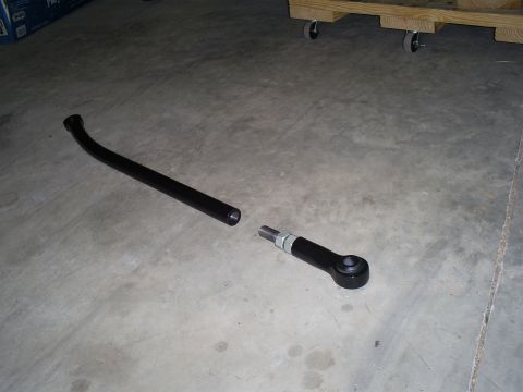 1992 Ford Bronco - A black tie rod assembly lies on a concrete floor next to a wooden pallet with wheels.