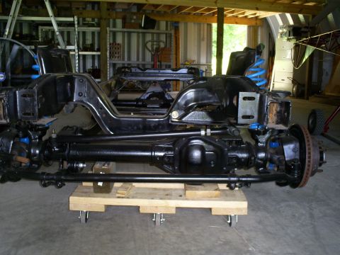 1992 Ford Bronco - Front axle and suspension parts are laid out on a wooden dolly in a garage.