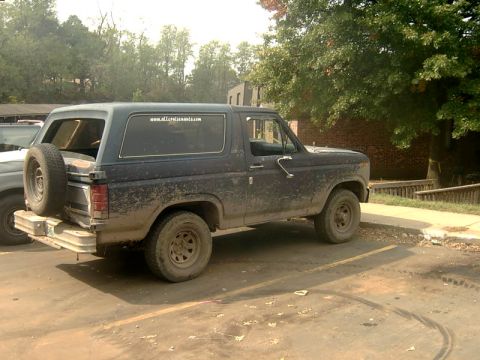 1982 Ford Bronco - A muddy 1982 Ford Bronco is parked on a dirt lot next to another vehicle.