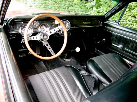1967 Mercury Cougar - The interior of a 1967 Mercury Cougar features a wood-rimmed steering wheel, black bucket seats, and a dashboard with prominent gauges.
