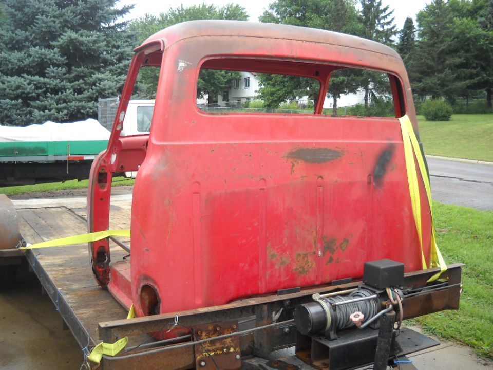 Red vintage truck cab strapped to a flatbed trailer outdoors