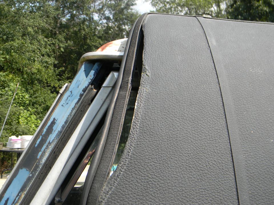 Close-up of a dark gray vinyl roof edge and peeling blue paint on a vehicle window frame