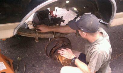 1990 Ford Bronco - Mechanic works on the rear brake assembly of a vehicle, possibly during maintenance or repair.