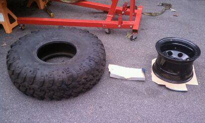 1990 Ford Bronco - A large off-road tire and a black steel wheel are laid out on the ground next to some equipment.