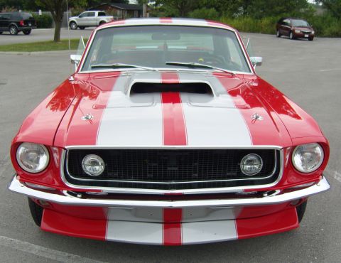 2007 Ford Mustang - A classic red and silver striped Ford Mustang is parked outdoors, viewed from the front.