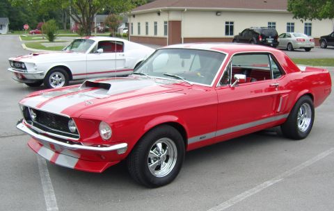 2007 Ford Mustang - Two classic Ford Mustangs, a red and a white model, are parked side-by-side in a lot.