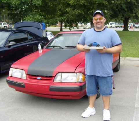 2007 Ford Mustang - A man stands with a model car in front of a red Ford Mustang at an outdoor car event.