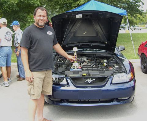 2007 Ford Mustang - A man holds a trophy next to a blue 2007 Ford Mustang at a car show.