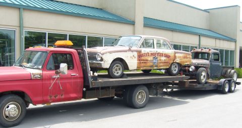 2007 Ford Mustang - A flatbed truck transports two old, weathered vehicles, a sedan and a pickup, down a street.