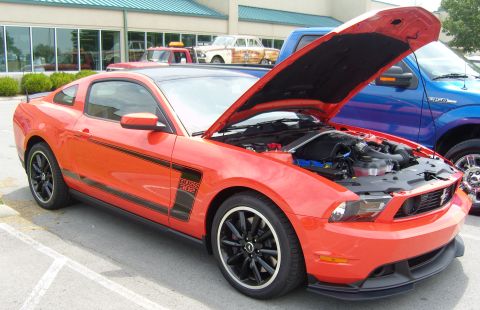 2007 Ford Mustang - Orange Ford Mustang with 'BOSS 302' graphics and its hood open is parked next to a blue truck.