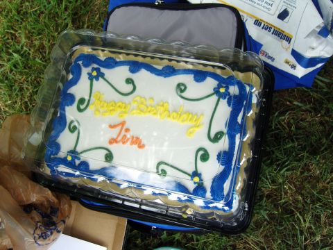 2007 Ford Mustang - A white cake with blue and yellow frosting, decorated with swirls and flowers, sits on a table outdoors.