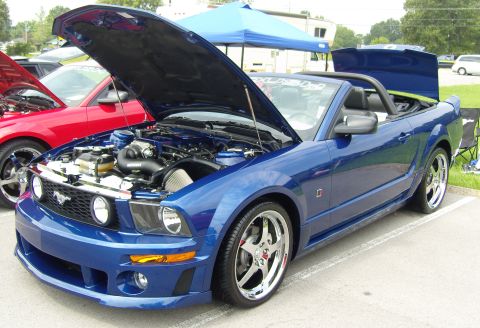2007 Ford Mustang - A blue convertible sports car is parked with its hood open, revealing the engine bay. Another vehicle is visible to its left.