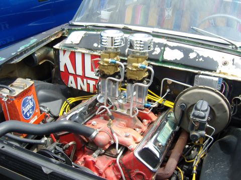 2007 Ford Mustang - The engine bay of a car shows a red engine block with dual carburetors and a can of oil.