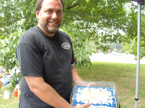 2007 Ford Mustang - A man holds a decorated cake outdoors with trees and grass in the background.