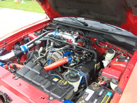 2007 Ford Mustang - Engine bay of a red 2007 Ford Mustang, an aftermarket cold air intake and custom blue engine component covers.