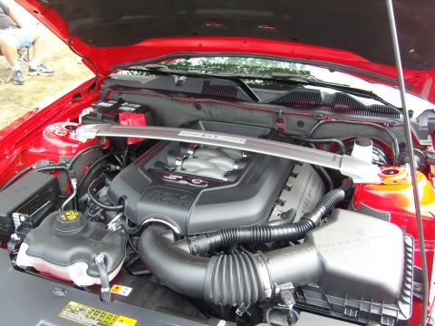 2007 Ford Mustang - The engine bay of a red Ford Mustang, the 5.0 V8 engine and intake system, with a strut bar across the top.