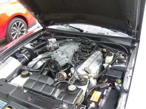 2007 Ford Mustang - The engine bay of a dark car, possibly a 2001 Ford Mustang, is shown with a red car in the background.