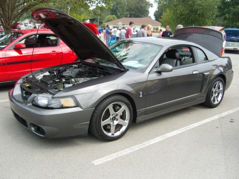 2007 Ford Mustang - A dark gray 2007 Ford Mustang coupe is displayed with its hood and trunk open, parked alongside a red Mustang at an outdoor car show.