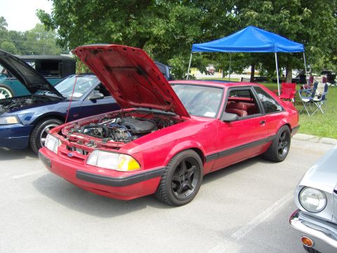 2007 Ford Mustang - A red Ford Mustang from the late 1980s is displayed with its hood up at an outdoor car show.